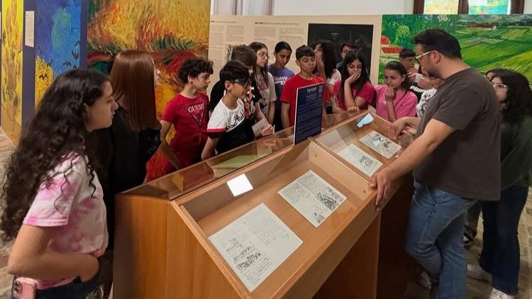 A group of students listening to a guide in front of a display case featuring Van Gogh’s letters and artworks.