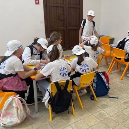 A classroom of children wearing white caps engaged in a creative workshop with drawings and colors.